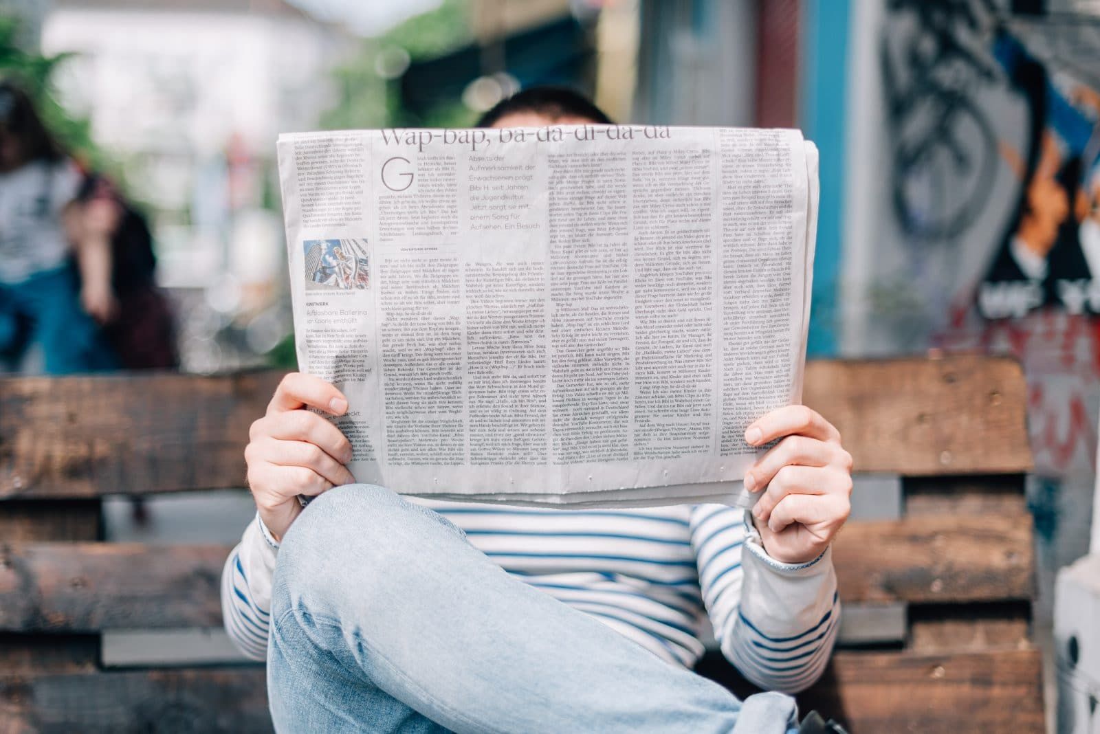 En person som sitter på en parkbänk och läser tidningen.